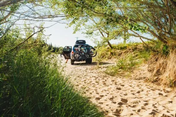 Car with bikes racked on the back parked on a sandy pathway.