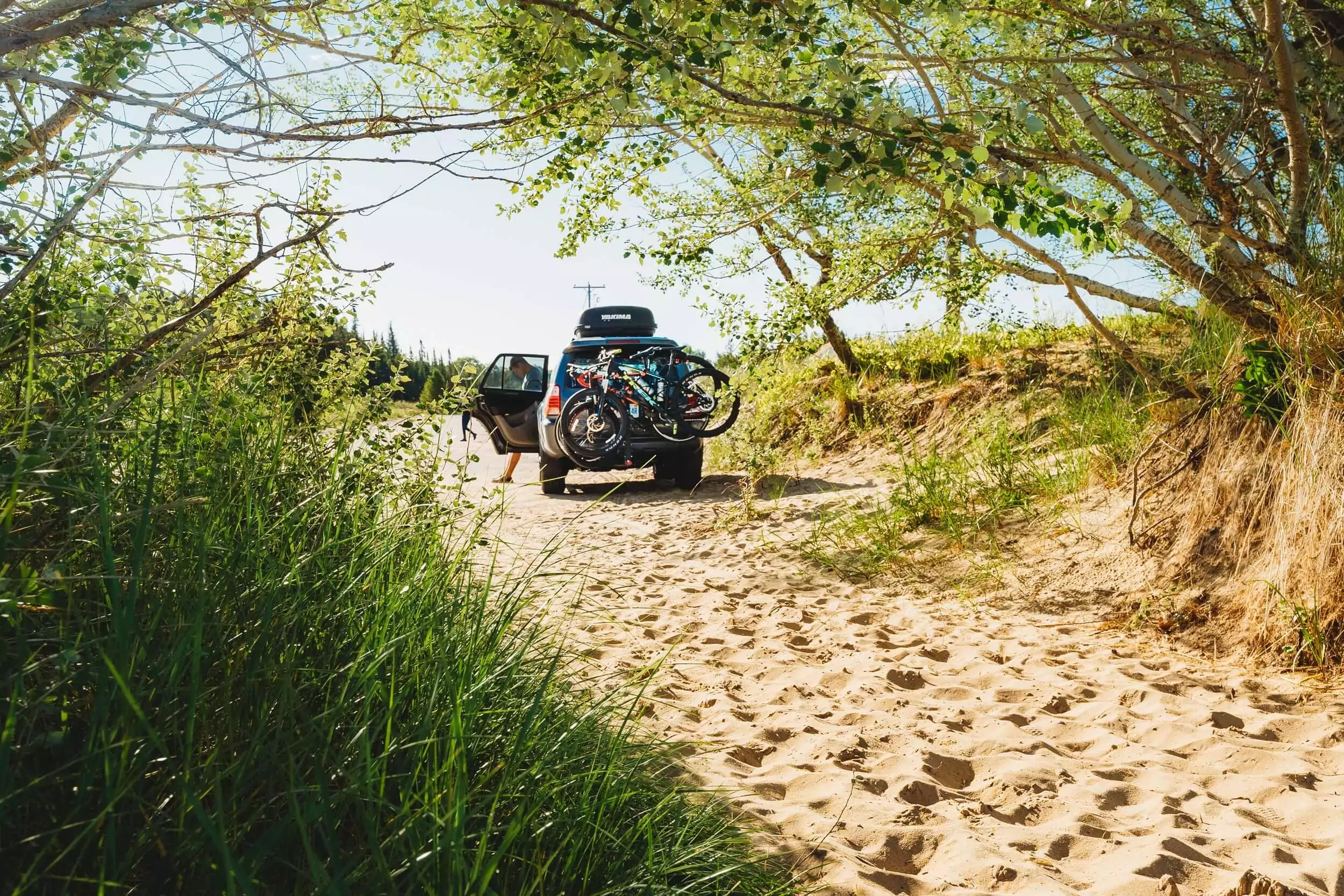 Car with bikes racked on the back parked on a sandy pathway.