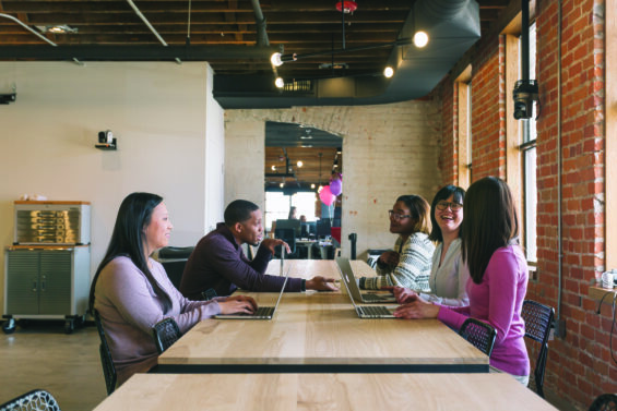 A group of coworkers gather around a table with laptops