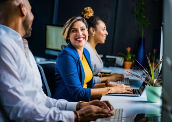 Woman in blue blazer smiles while speaking with coworker to her right.