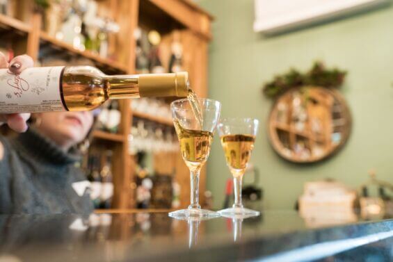 Woman pours ice wine into two glasses that rest on a bar top.