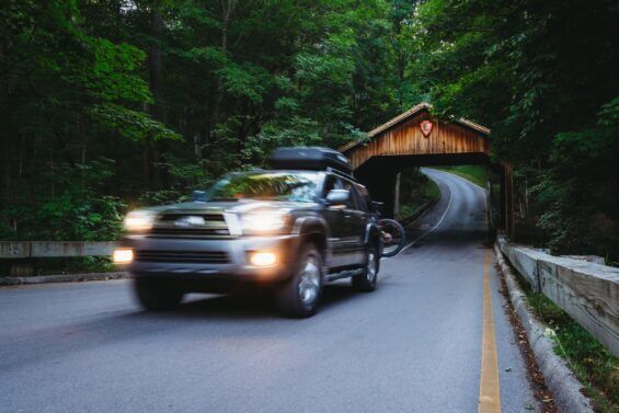 Car driving down smooth road with green trees on both sides.