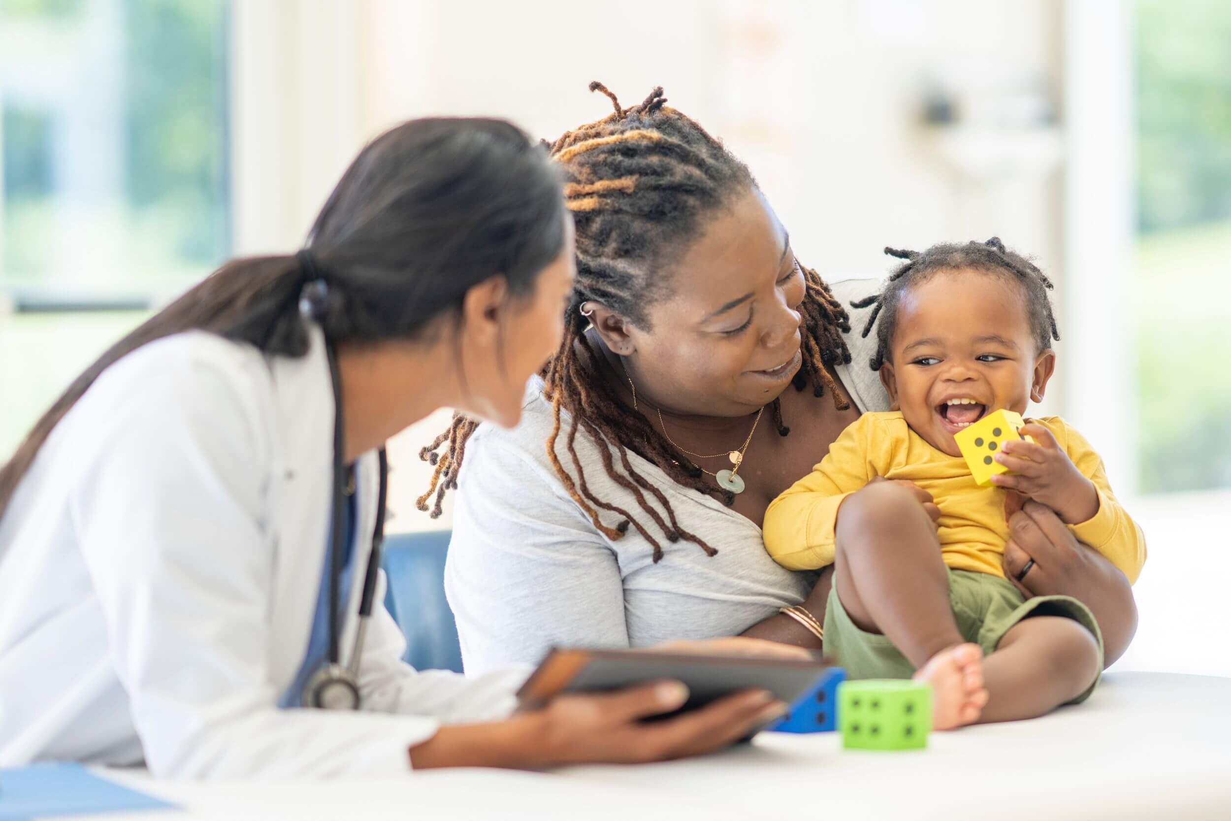 Mother holds smiling baby while talking to pediatrician