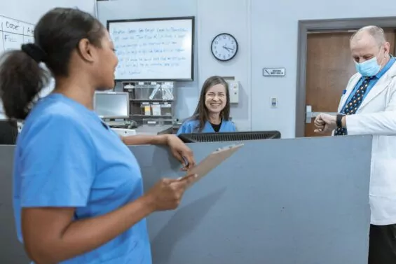 Two nurses and a doctor smile at their desk.