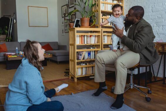 Father holding baby on his lap while he smiles at the mother sitting on the floor.