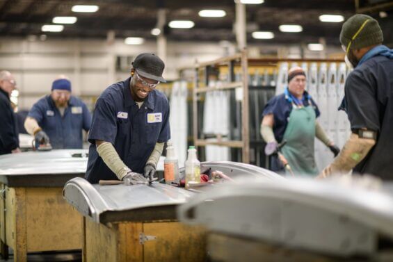 Young man smiles while sanding down a metal piece in a metal craft's workshop.