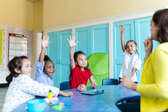 Group of young, female students raising their hands to answer a question.