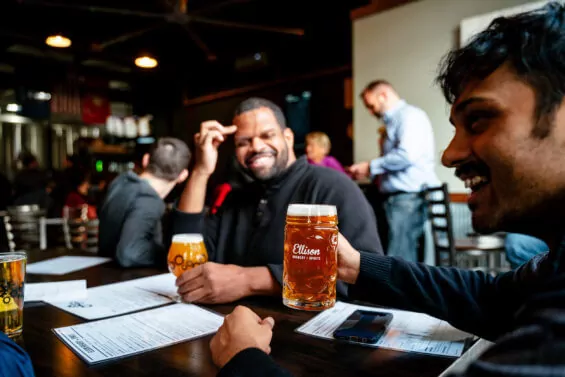 Two friends laugh while drinking beers at a brewery.