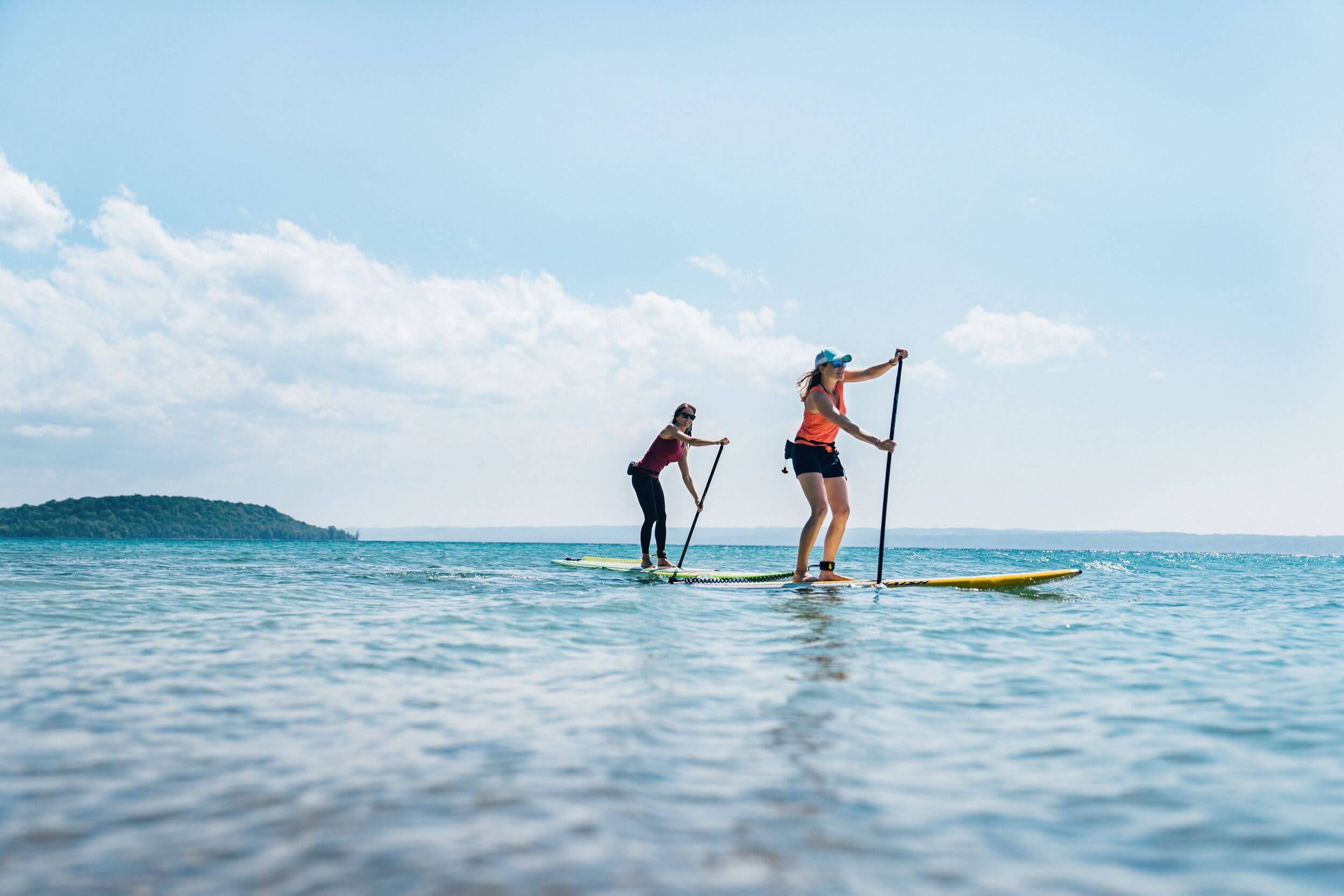 Two women paddleboard in Grand Traverse Bay on a sunny day.
