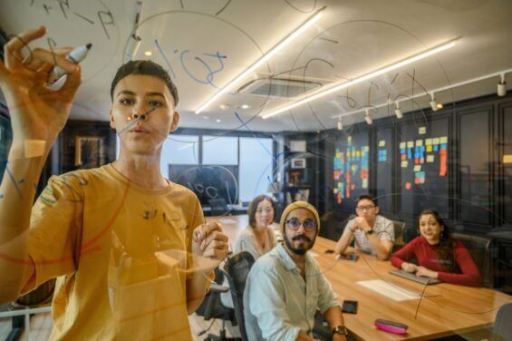 Group of students watch classmate take notes on glass wall.