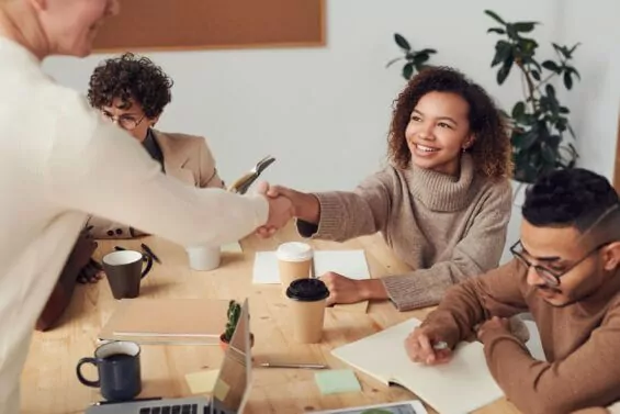 Young woman shakes hands at conference table.
